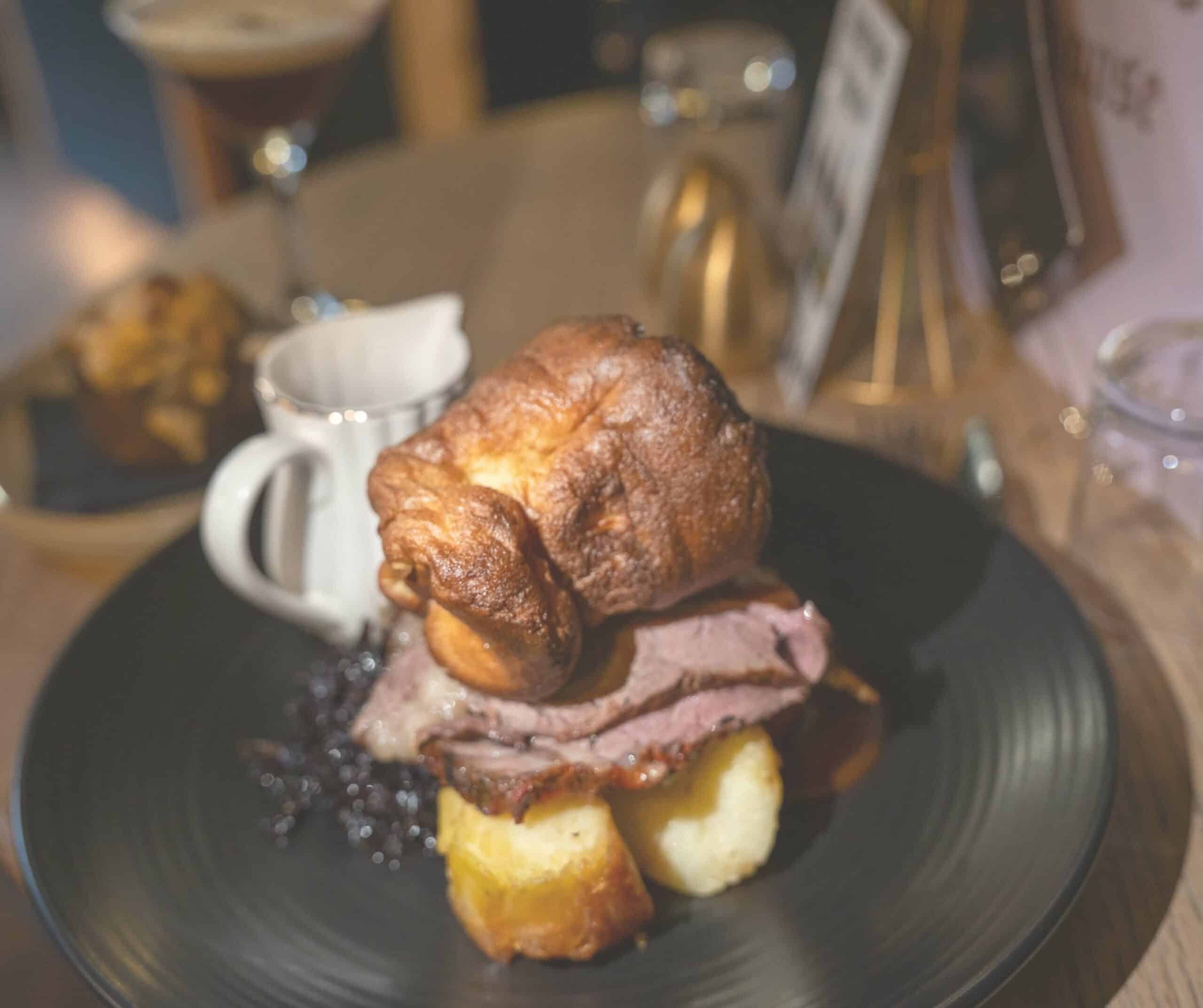 Sunday roast at Fletcher's House in Rye with sliced beef, a tall Yorkshire pudding, roast potatoes, and a jug of gravy