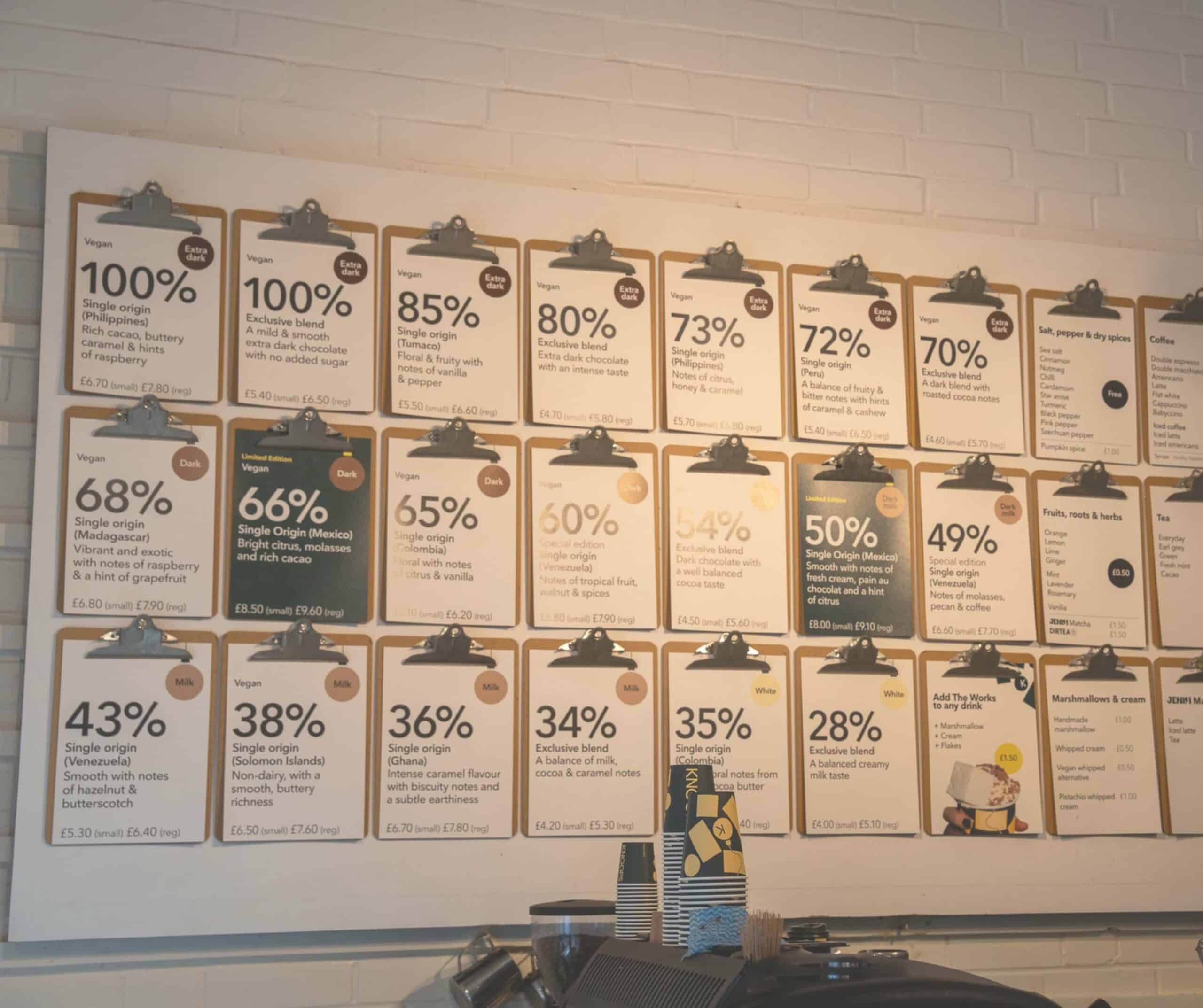 Knoops chocolate menu wall in Rye with clipboards showing cocoa percentages from 28% white to 100% dark and their tasting notes