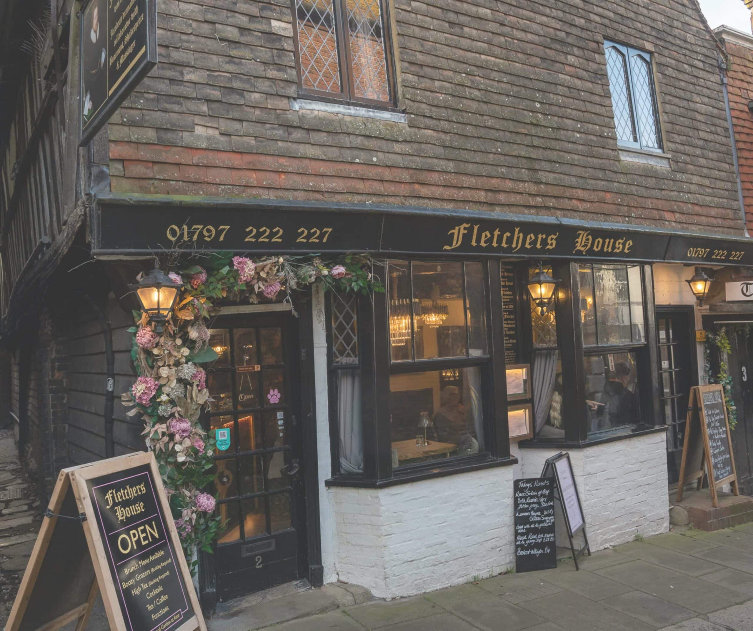 Fletcher's House storefront in Rye, a historic Tudor building with a black facade, lantern lights, and floral door display