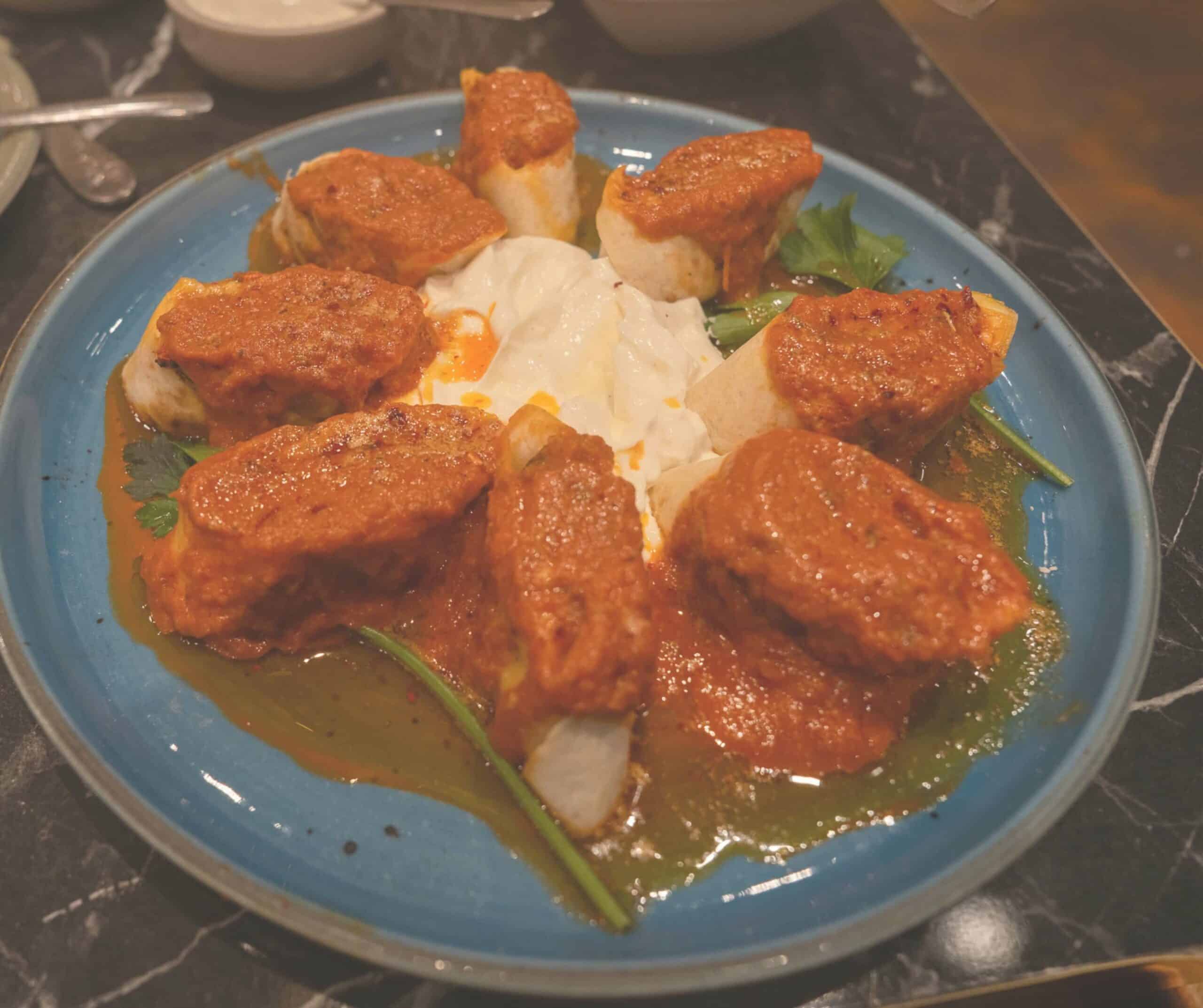 Beyti kebab at Diamond Köz in Rye, lamb wrapped in flatbread topped with tomato sauce and served over yogurt on a blue plate