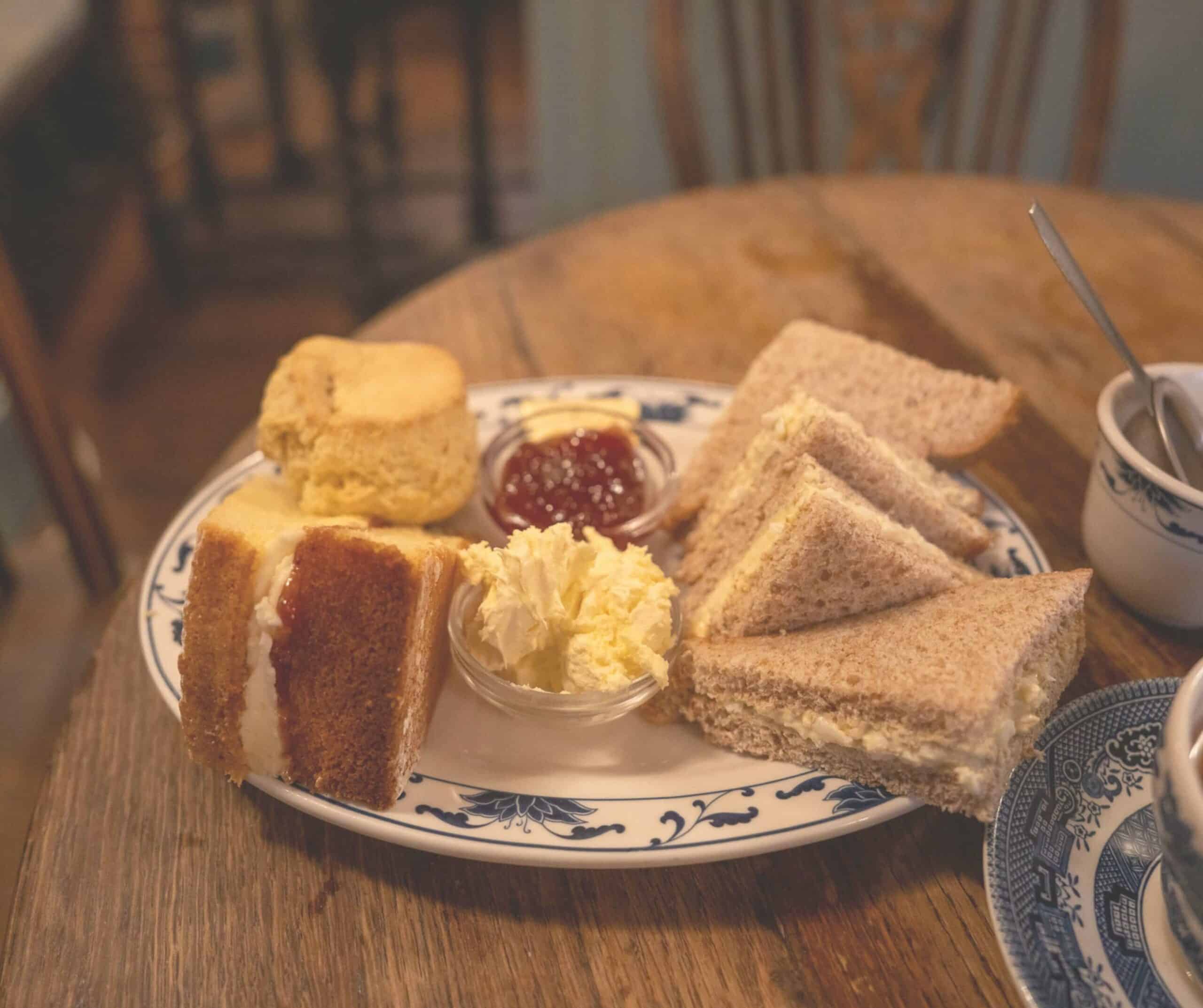 Afternoon tea at The Cobbles Tea Room in Rye with a scone, jam, clotted cream, Victoria sponge, and egg sandwiches on blue china