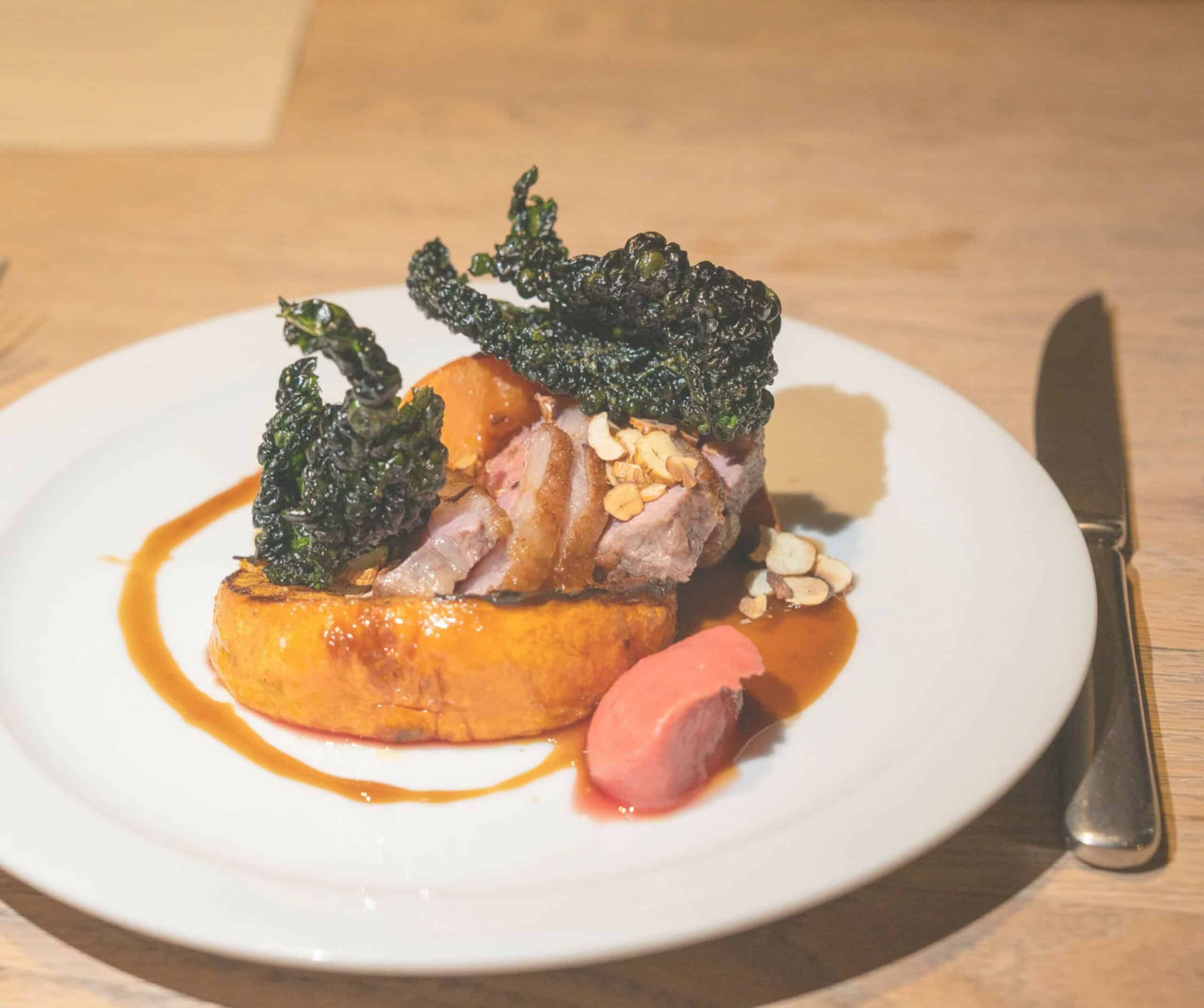 Pork dish at The Union in Rye with roasted squash, crispy kale, hazelnuts, and pan juices on a white plate