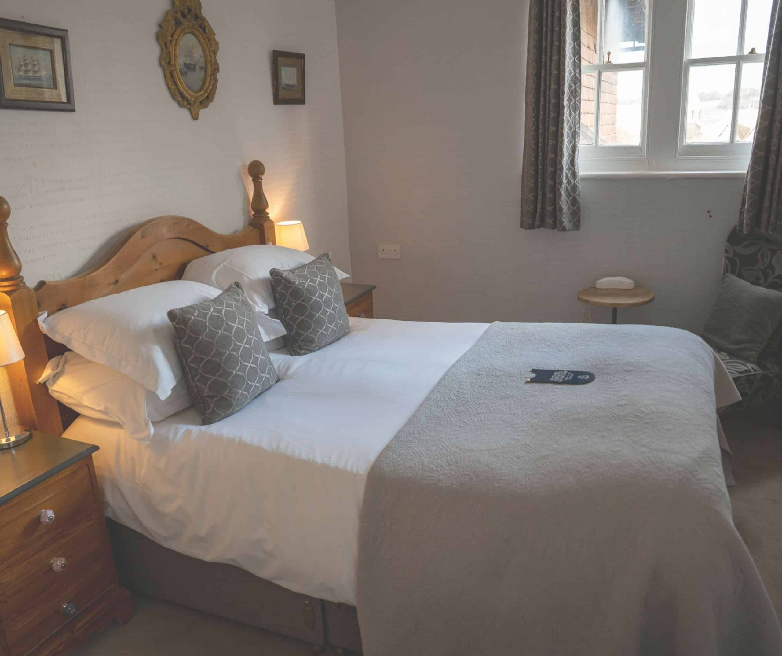 Cozy bedroom at the Hope Anchor Hotel in Rye with a pine bed, white linens, and nautical prints on the wall