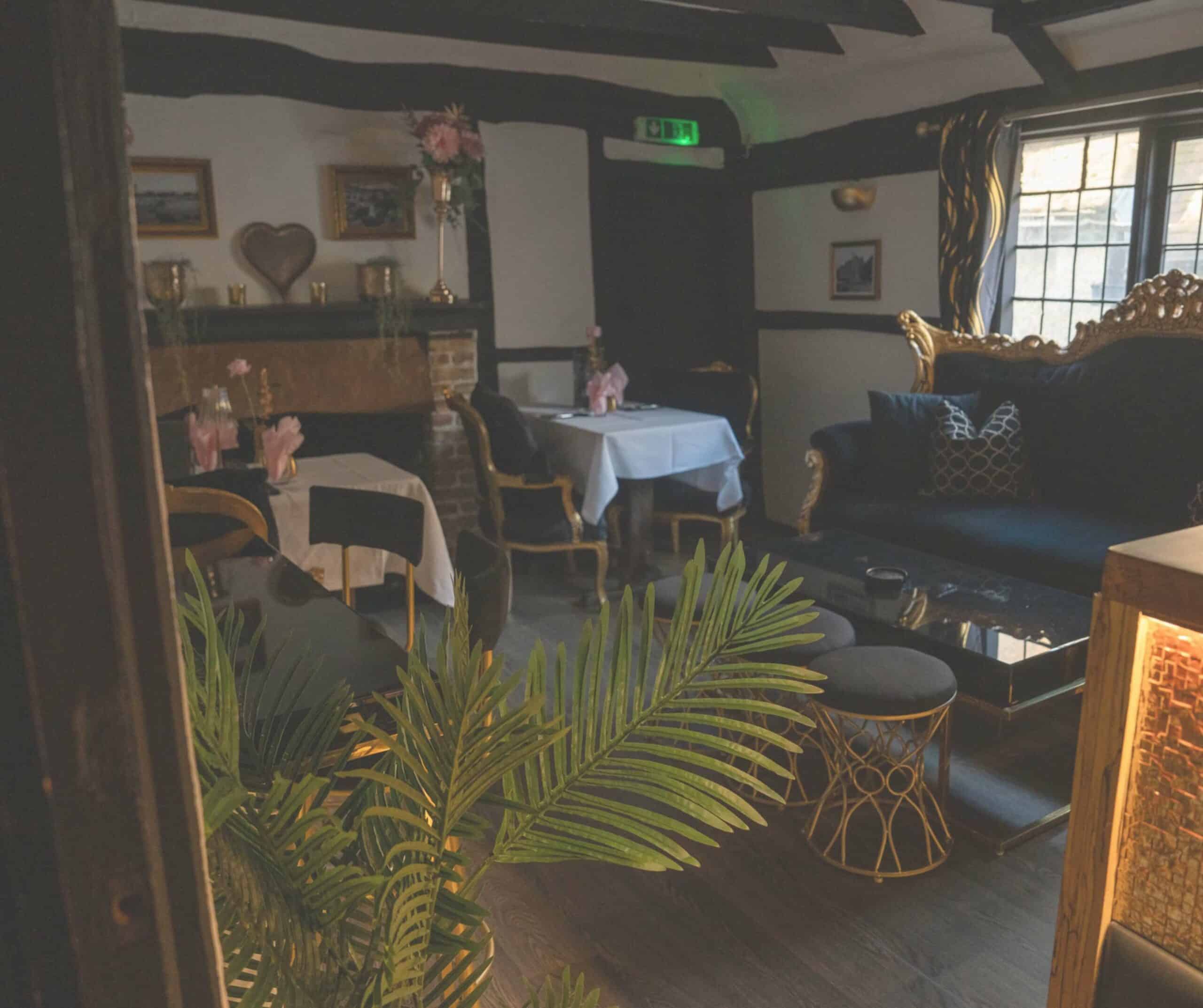 Interior of Fletcher's House in Rye with exposed Tudor beams, gold-framed art, velvet sofa, and white-clothed tables