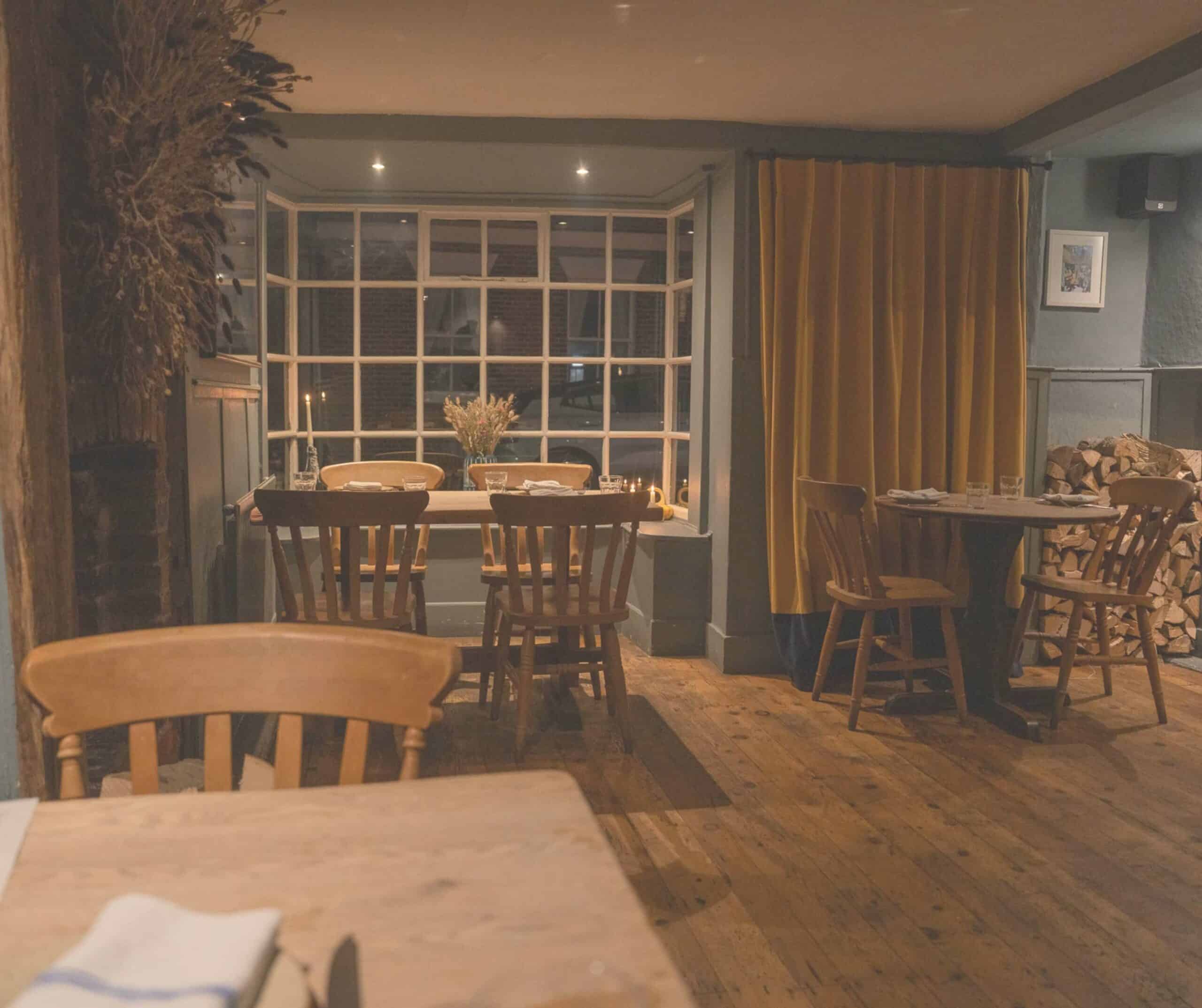 Cozy candlelit interior of The Union in Rye with wooden tables, window seats, and a stack of firewood