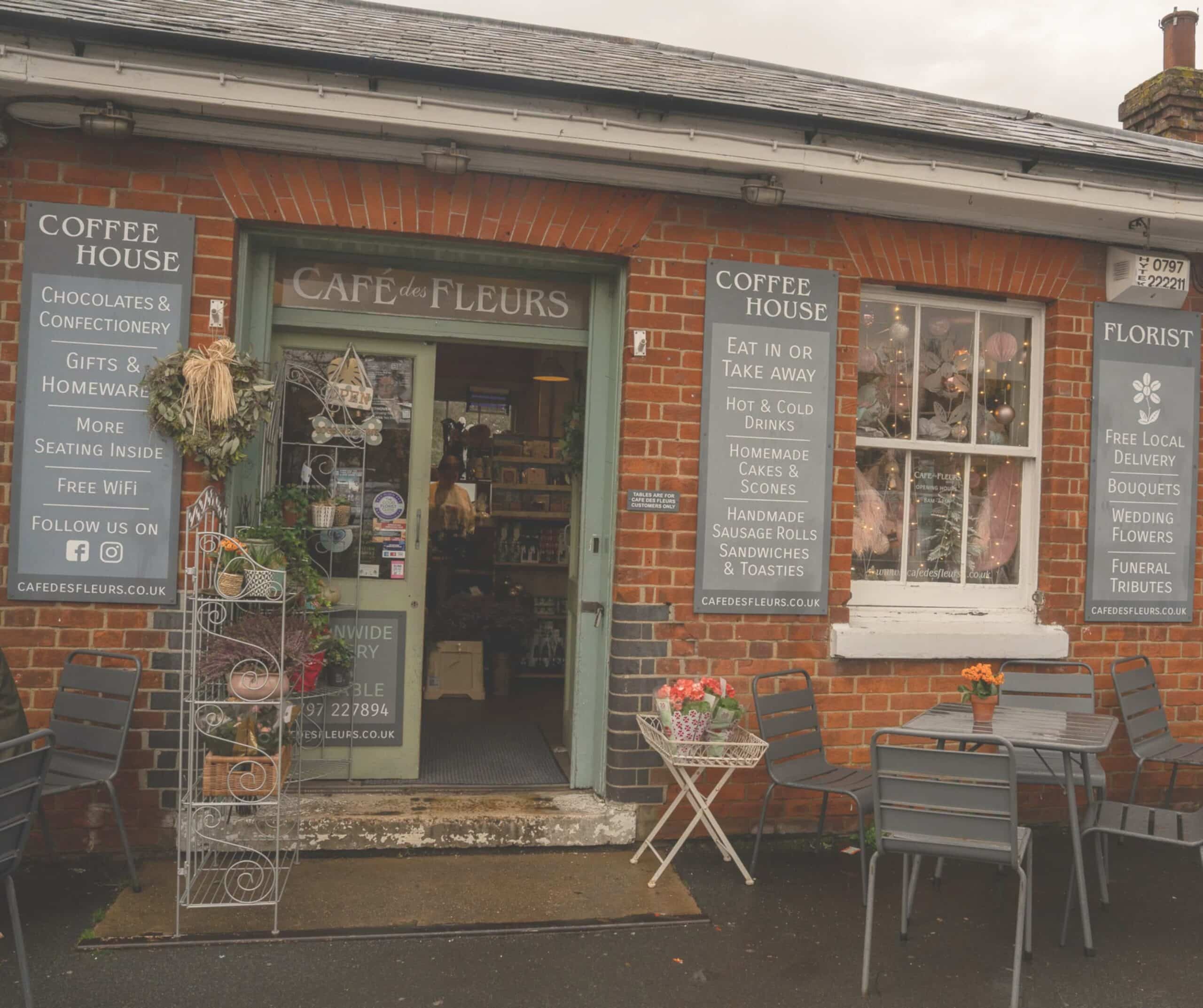 Brick storefront of Café des Fleurs next to Rye railway station, with painted coffee house and florist signs and outdoor seating