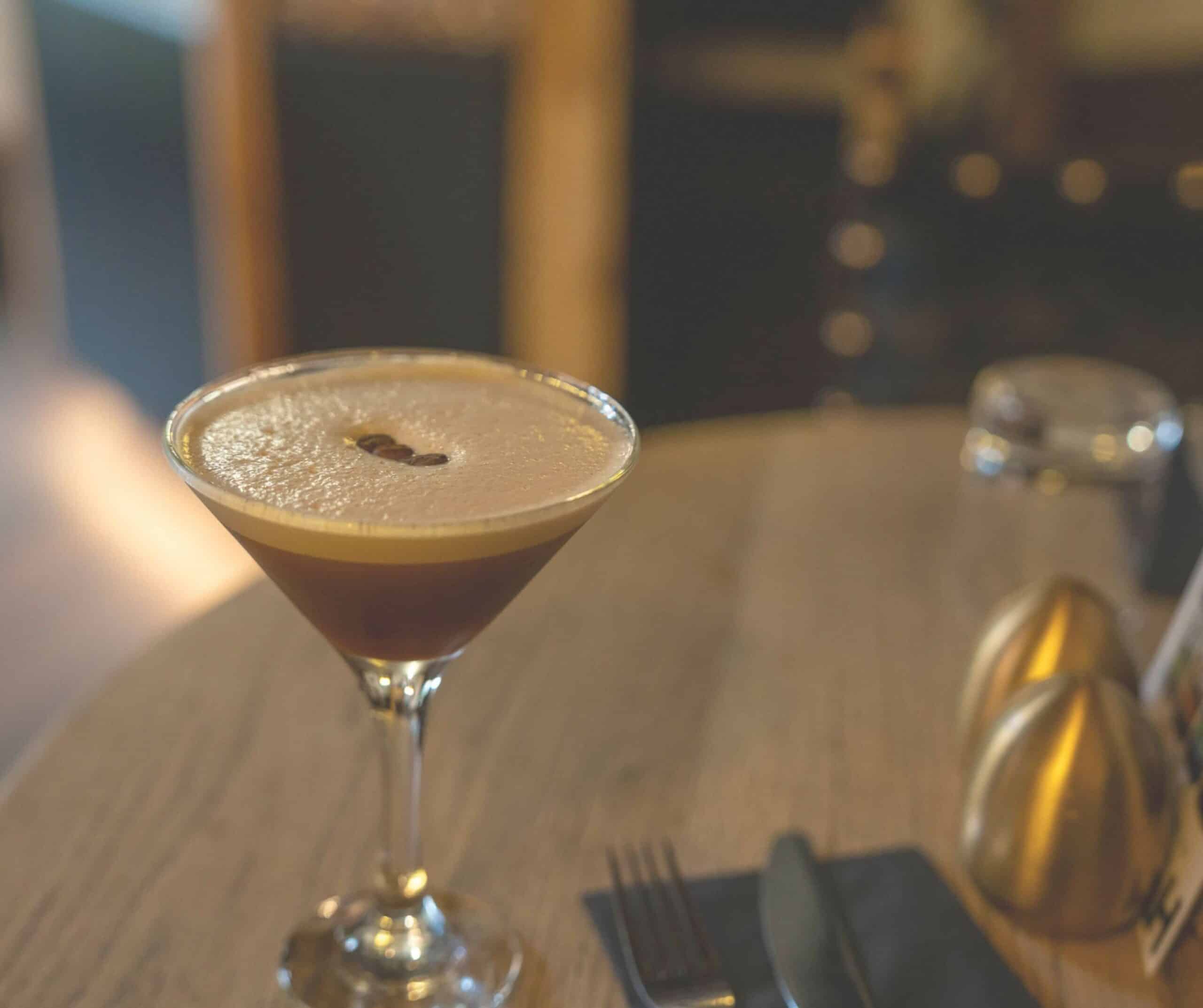 Espresso martini topped with coffee beans in a martini glass on a wooden table at Fletcher's House in Rye