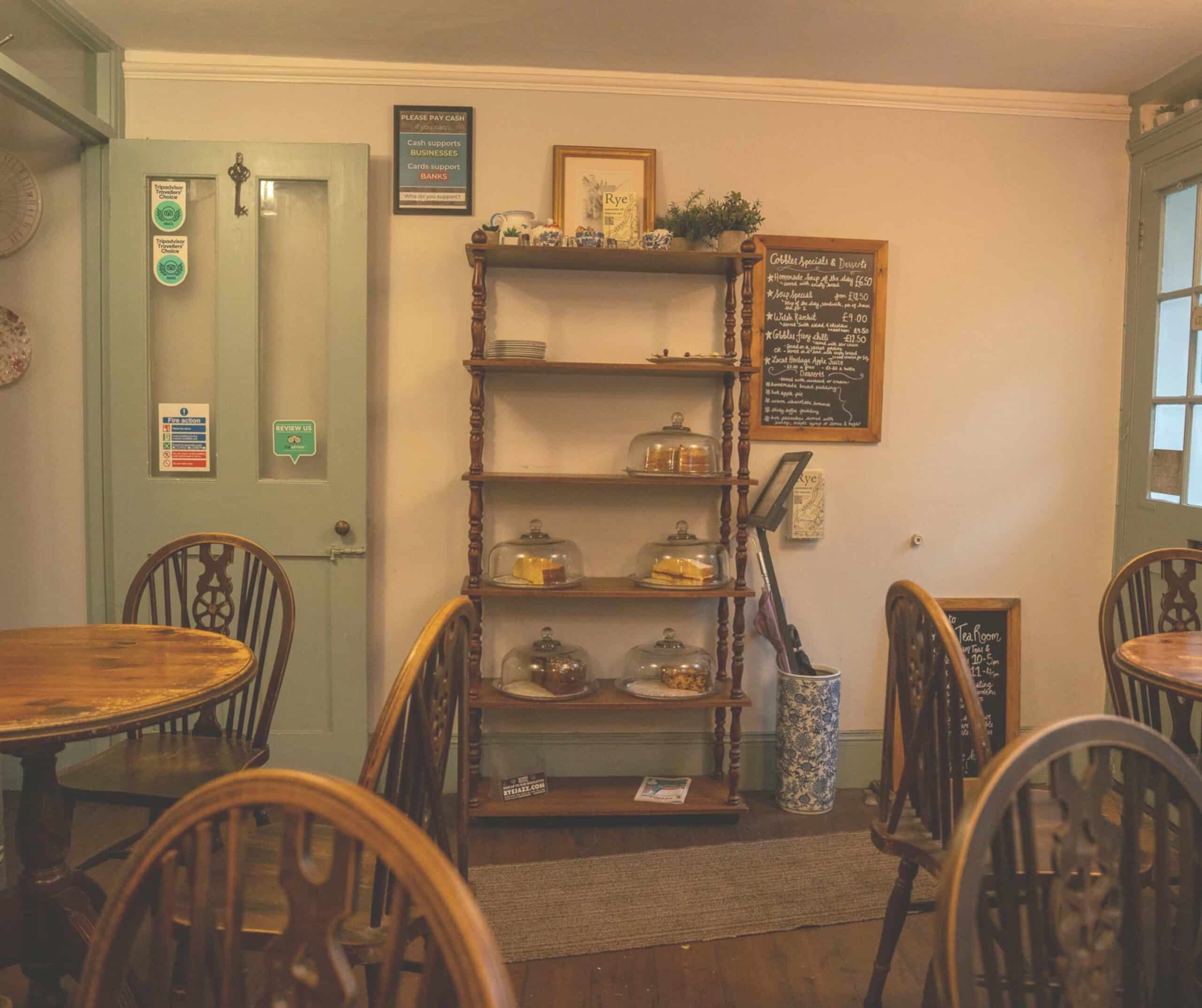 Interior of The Cobbles Tea Room in Rye with a wooden cake shelf, chalkboard specials menu, and Windsor chairs