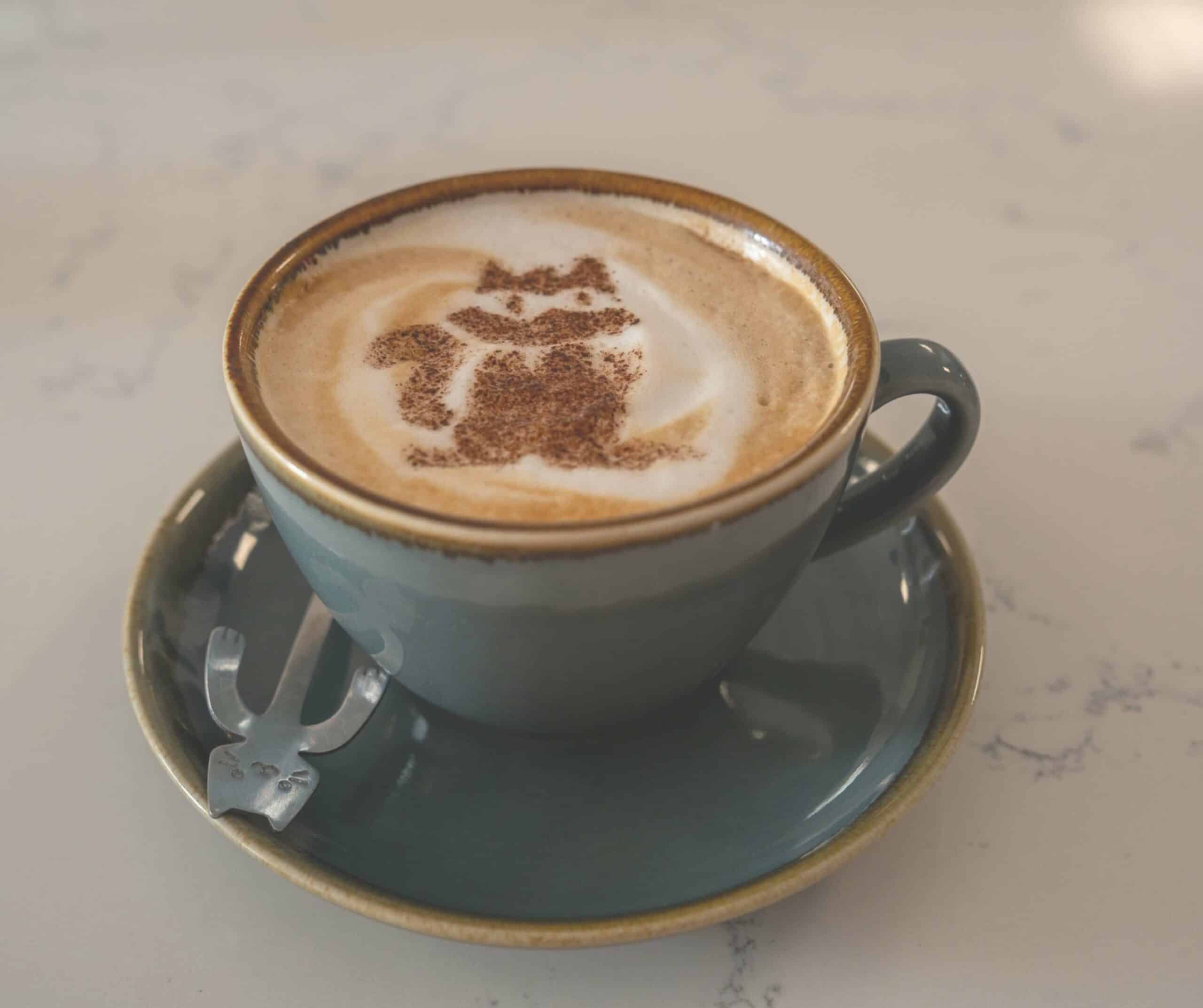 Cappuccino with cat-shaped cocoa art and a cat-shaped spoon at Kiko's Cat Cafe in Rye