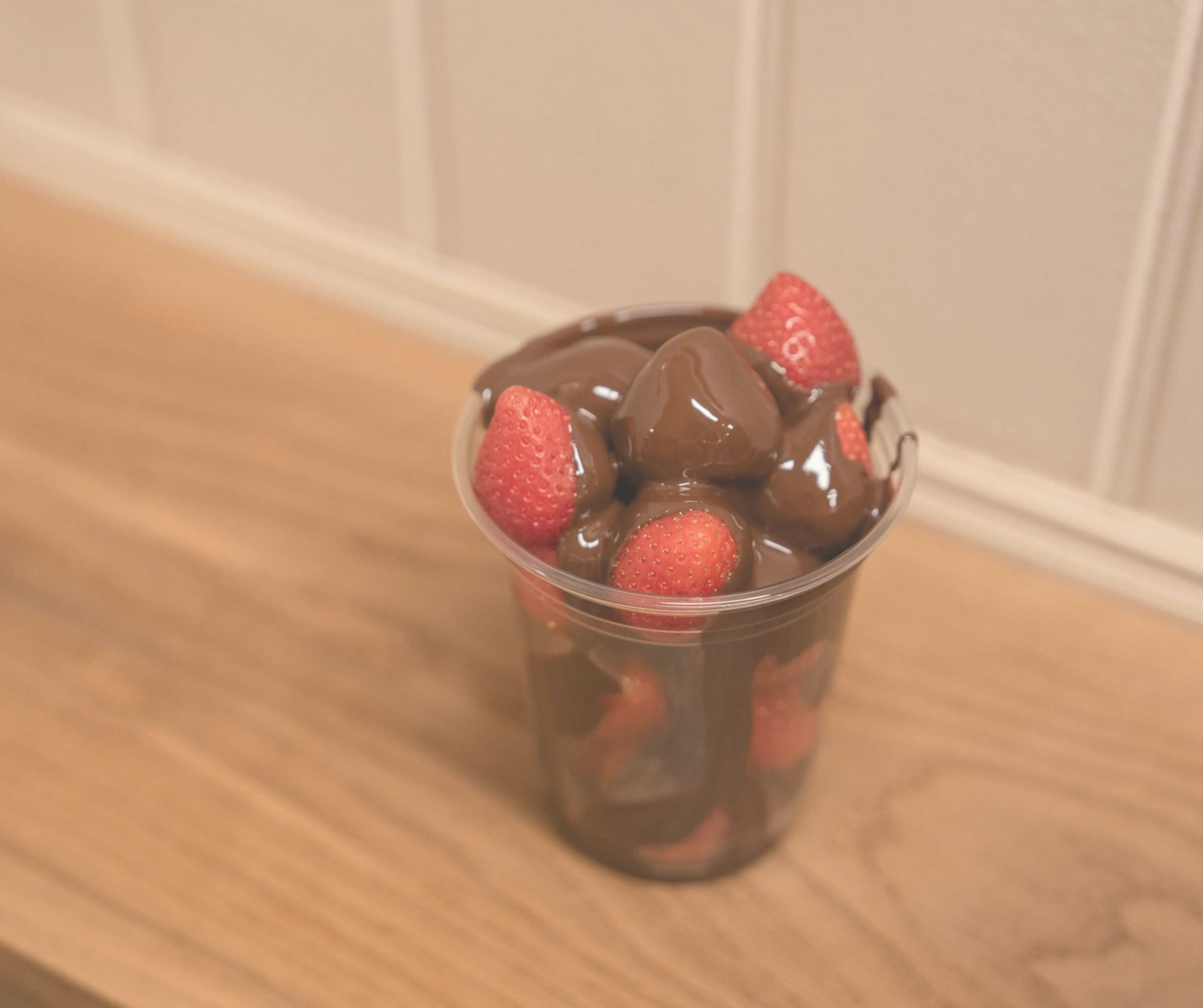 Cup of fresh strawberries covered in melted Belgian chocolate from Cocoamore in Rye, served on a wooden table