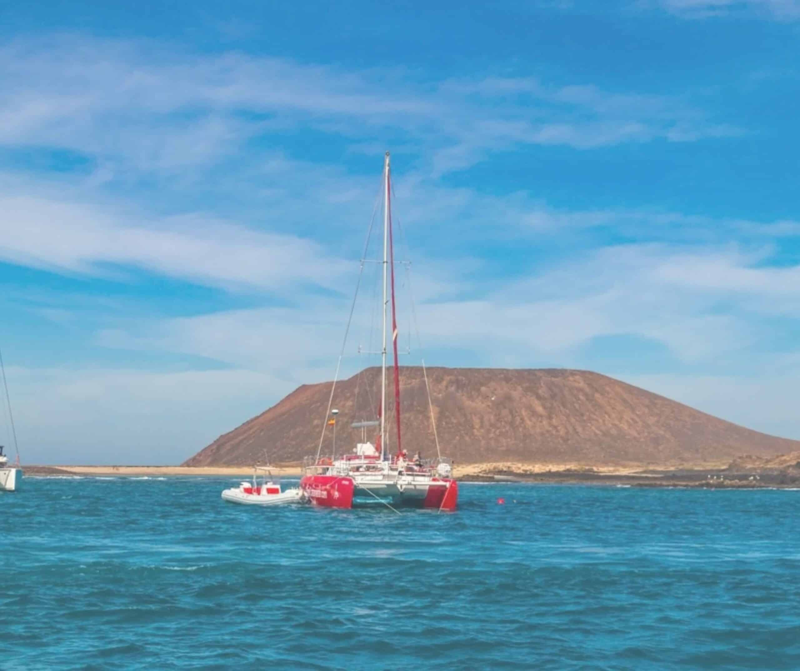 Red sailing catamaran anchored off Lobos Island near Corralejo, Fuerteventura, with the island's volcano behind it
