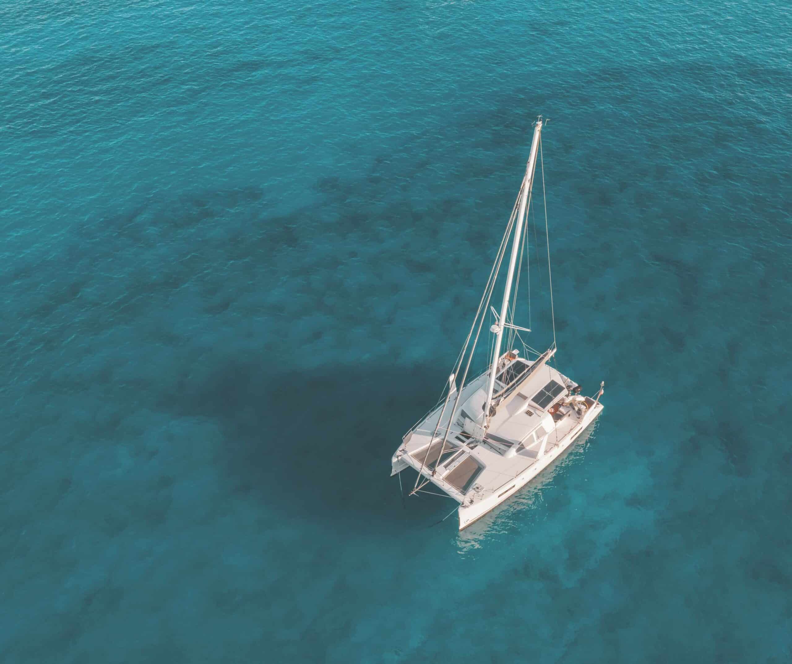 Aerial view of a white sailing catamaran anchored in clear turquoise water, like the boats on adults-only Lobos Island trips