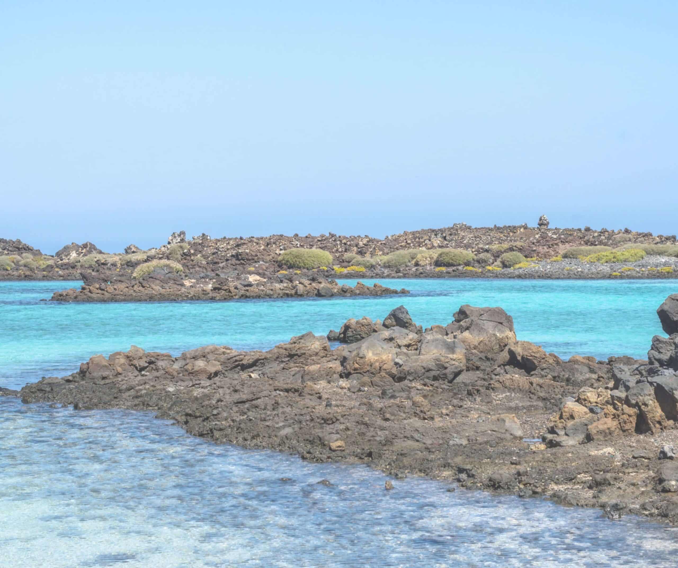 Clear turquoise water between dark volcanic rocks on the coast of Lobos Island, Fuerteventura