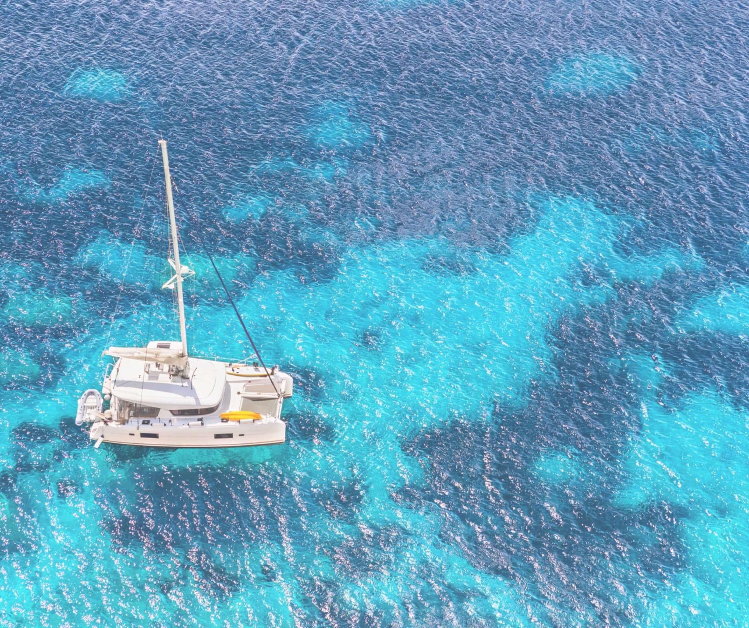 Aerial view of a private catamaran with kayaks and a paddleboard on deck, anchored in clear turquoise water